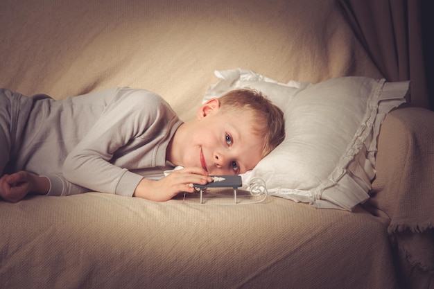 The boy lies with a Christmas toy in bed and looks into the camera Waiting for the holiday