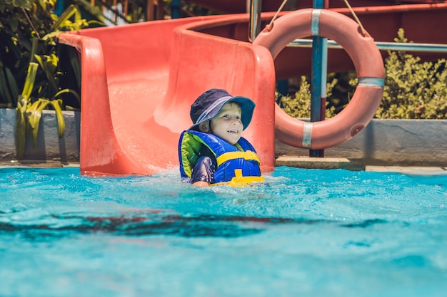 A boy in a life jacket slides down from a slide in a water park.