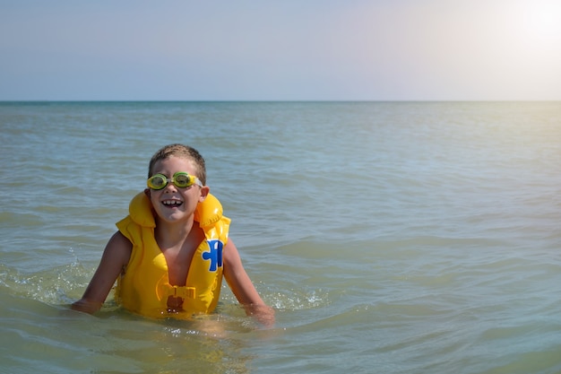 水中で救命胴衣を着た少年。うれしそうな子供は晴れた日に海で夏休みを過ごします。バナー