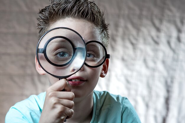 Boy in a light t-shirt and glasses looking into a large magnifying glass