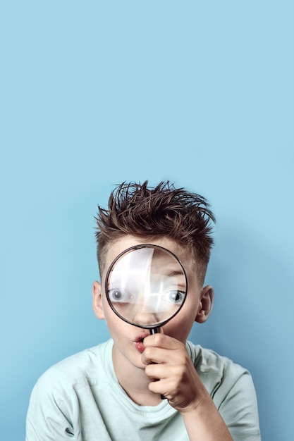 Boy in a light t-shirt looking into a large magnifying glass