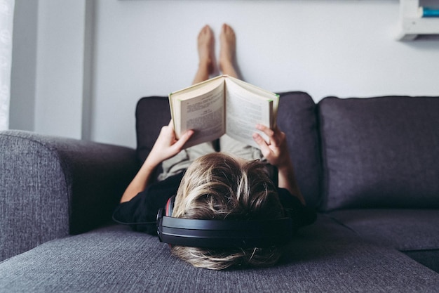boy listening music while reading book on sofa at home