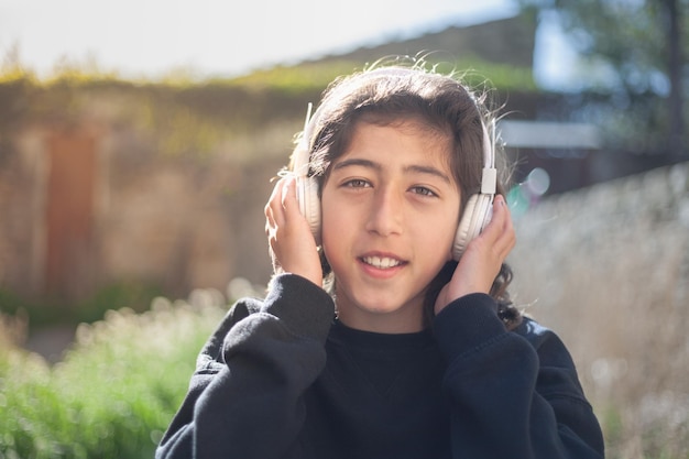 Boy listening to music with white headphones outside next to a green meadow