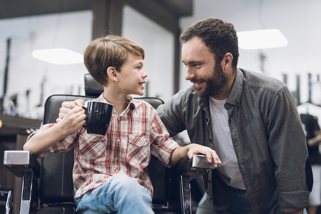 The boy listens to an adult man sitting in a barbershop.