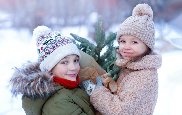 A boy and a little girl with an armful of fir branches are looking into the camera and smiling again