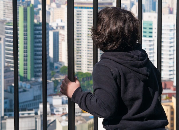 Boy looking to the city behind the bars.