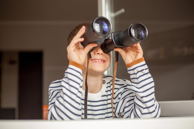 Photo boy looking through binoculars while standing by window