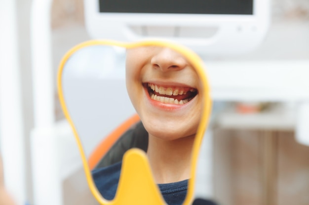 少年は歯科医院の歯科医と一緒に椅子に座って歯を見せる笑顔で鏡を見る