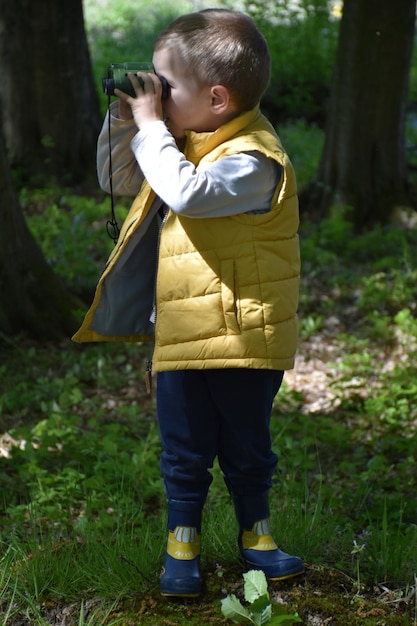 Photo the boy looks through binoculars in the woods