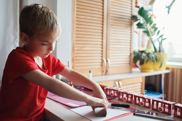 Boy makes crafted advent calendar on theme of skis and cable car with toilet paper rolls at home