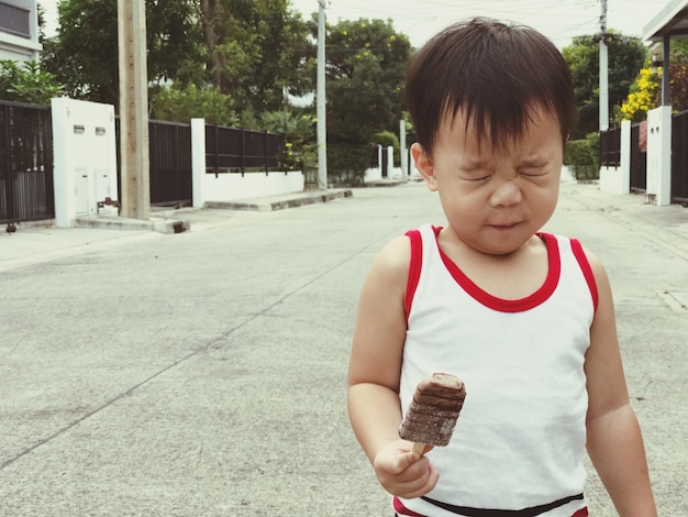 Photo boy making face while holding ice cream on street in town