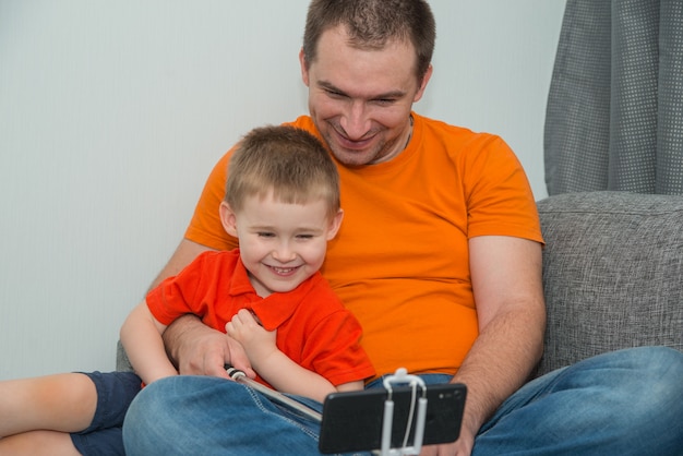 Boy and man in bright clothes looking in the smartphone during online call and smiling. Stay home and distance communications concept