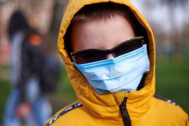 Foto ragazzo con maschera medica e occhiali da sole nel parco primaverile