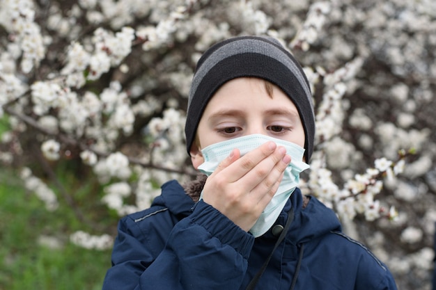 Boy in a medical protective mask outdoors. Flowering tree, spring day