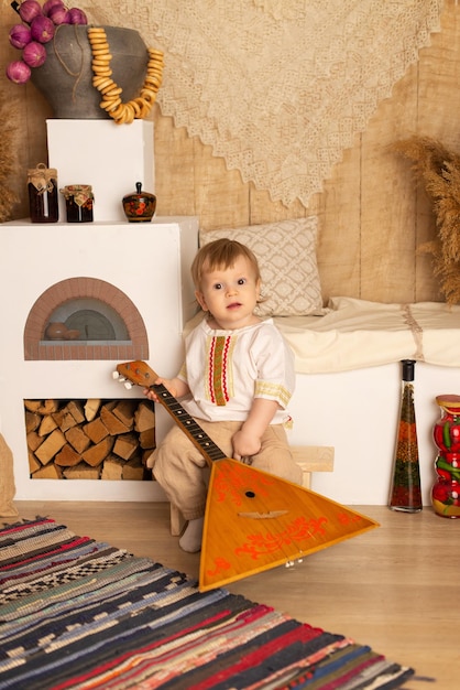 A boy in a national costume is sitting with a balalaika Pancake day