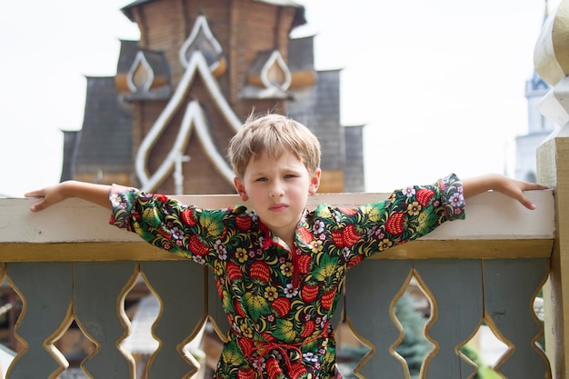 The boy in the national Russian clothes on the background of wooden buildings