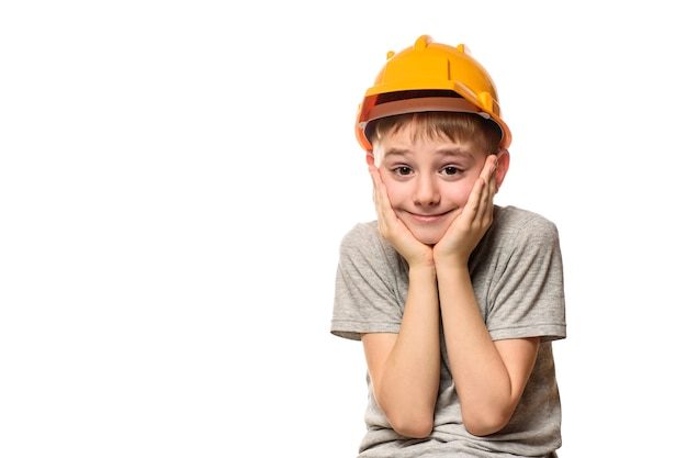 Boy in orange construction helmet put hands on cheek. Portrait. Isolate on white wall.