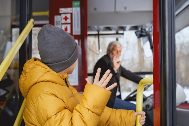 Boy in orange jacket holding handrail waving to driver while getting off bus