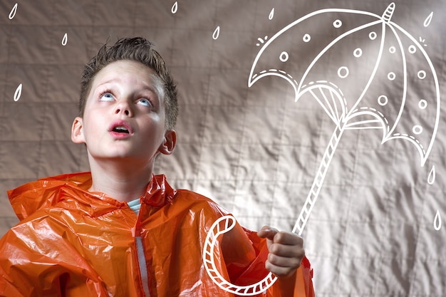 オレンジ色のレインコートと塗られた傘を持つ少年は雨の中で立ちます