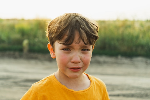 オレンジ色のTシャツを着た男の子が自然の中で泣いています