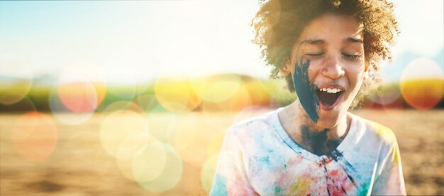 Photo boy outdoor and paint splash on face with mockup space by field grass or nature for holiday in blurred background young happy kid sunshine and excited smile at park game or countryside vacation