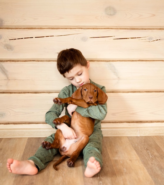 A boy in pajamas plays with a puppy in a wooden house