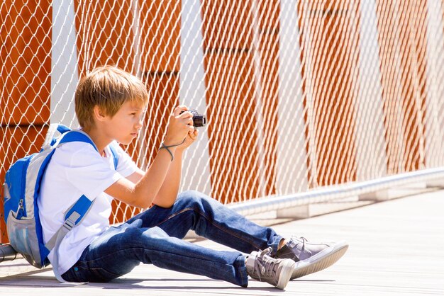 Boy photographing while sitting on footbridge in city