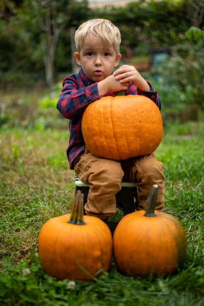 Boy in a plaid shirt sits in the garden among pumpkins