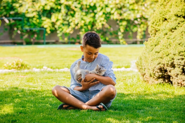 Photo boy play with adorable gray kitten outdoors