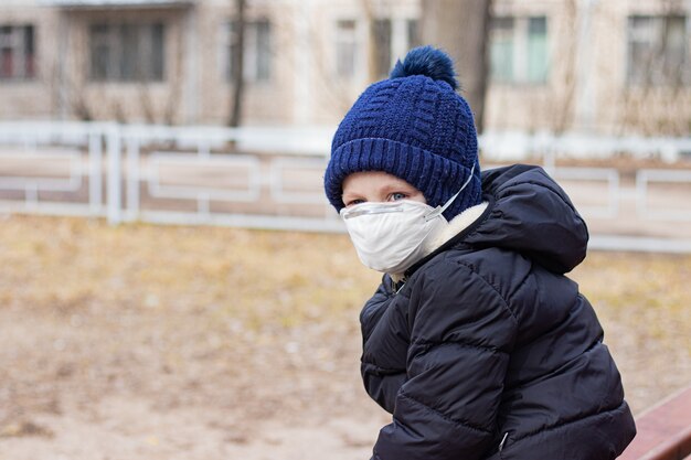 仮面の遊び場にいる少年。健康。コロナウイルス。子供の顔に医療用マスク。セキュリティ。肺炎とインフルエンザ。呼吸保護。