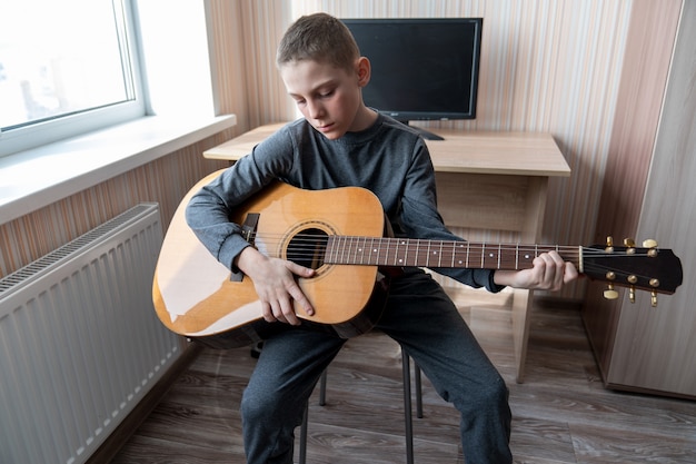 Boy playing acoustic guitar sitting by the window