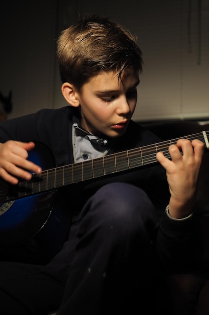 A boy playing a blue guitar in a dark room.