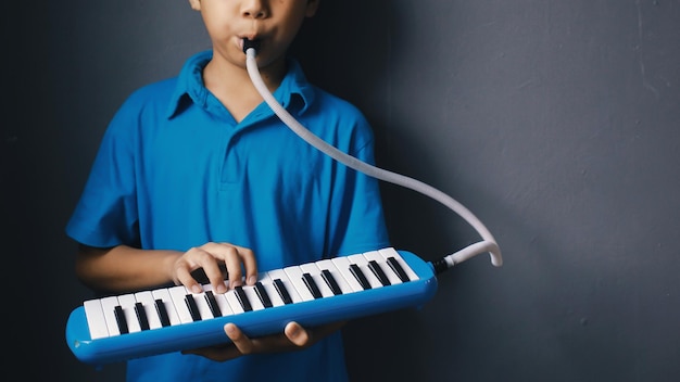 Photo boy playing blue melodeon musical instrument melodica blow organ pianica or melodion in dark gray