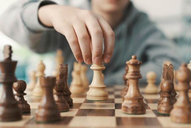 Boy playing chess and moving a piece hand close up