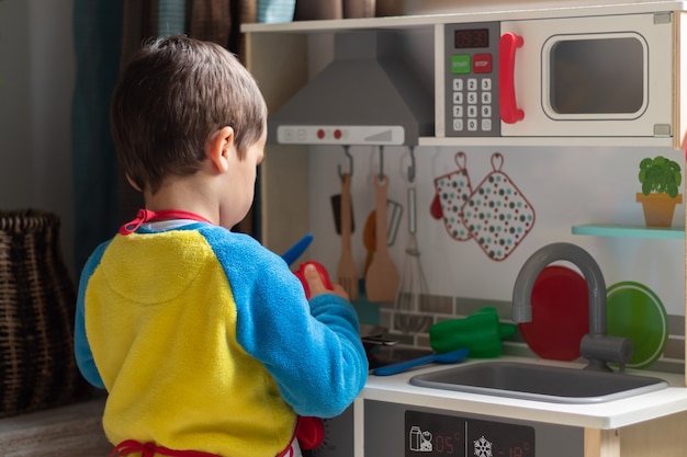 Boy playing cook with a toy kitchen at home