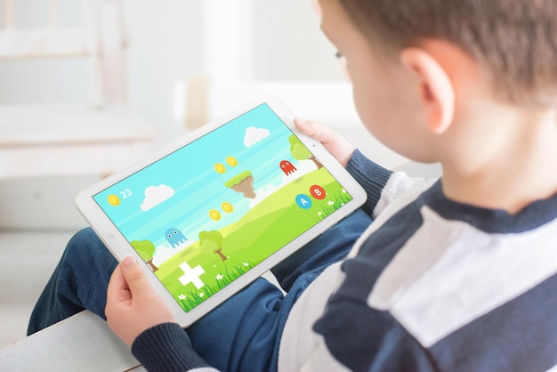 Boy playing game on white tablet Home interior in bacgkround Kid games on mobile devices concept