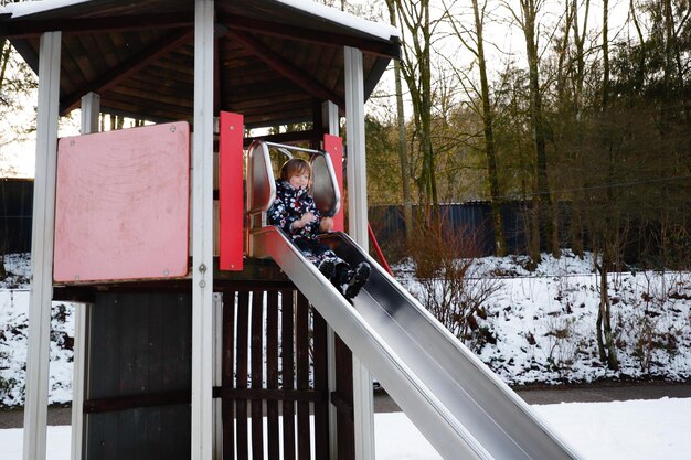 Photo boy playing on slide over snow covered playground