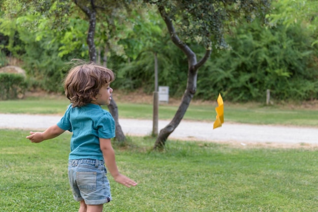 目をそらしてトス紙飛行機を遊んでいる少年週末に楽しんでいる春と夏の公園で遊んでいる陽気な白人の少年の肖像画