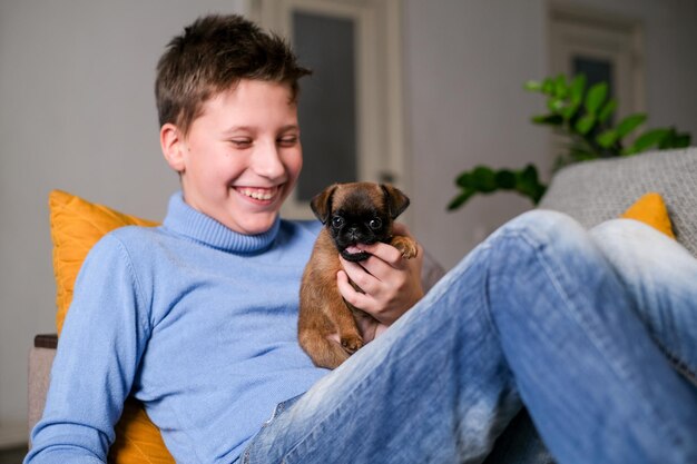 Boy playing with baby dog. Kid play with puppy at home. Little boy and griffon or brabanson dog