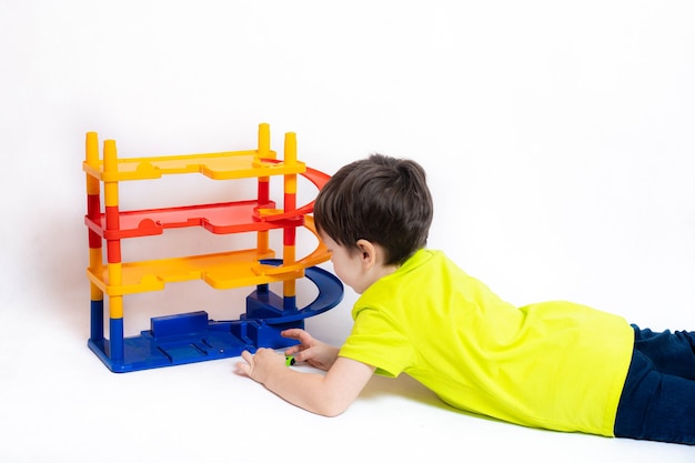 Boy playing with cars in the Parking lot . Children's toy . A boy plays with toys on a white wall. Bright Parking for cars. Happy childhood