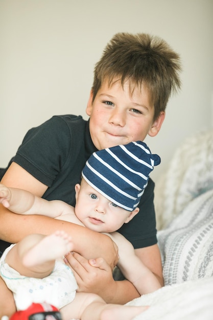 Photo boy playing with his baby brother at home siblings with big age difference school child hugging little sibling