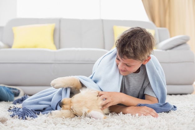 ラグに横たわっている子犬で遊んでいる少年