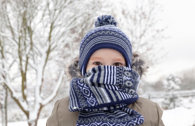 写真 冬の雪で遊ぶ少年。子供は霜のためにスカーフに隠れました。降雪後の白い雪に覆われた公園内の場所。写真のクローズアップ。