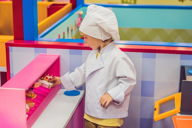 Мальчик играет в игру, как если бы он был поваром или пекарем на детской кухне.