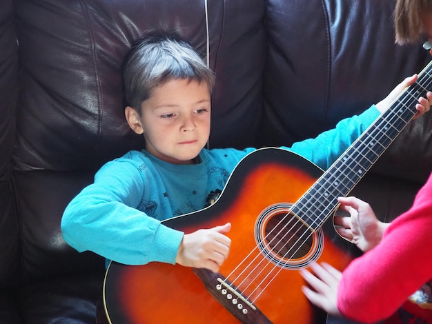 A boy plays a guitar on a couch.