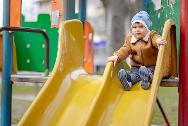 The boy plays on the playground and rides a slide in autumn weather