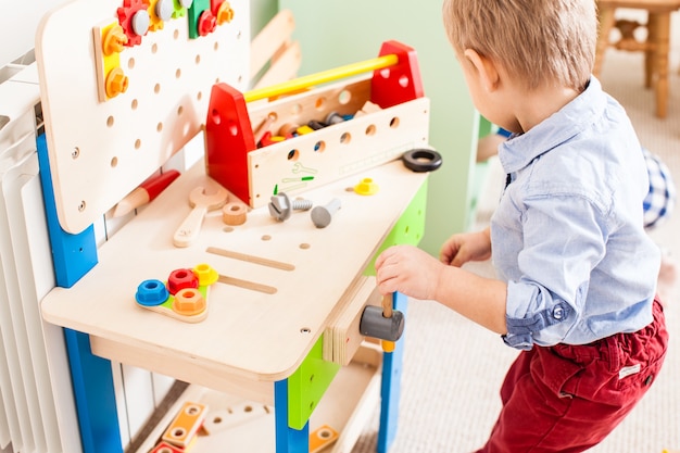 Boy plays with builder wooden instruments in the kindergarten