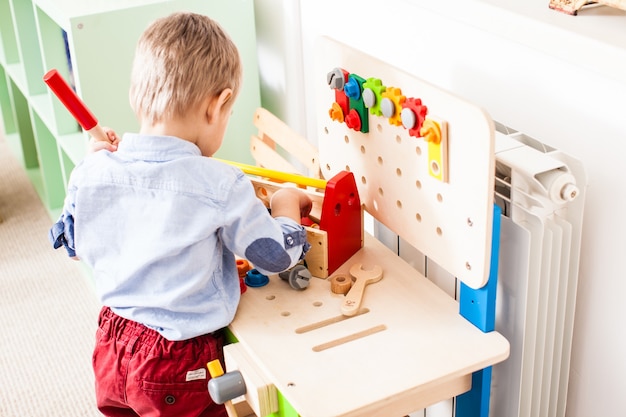 Boy plays with builder wooden instruments in the kindergarten