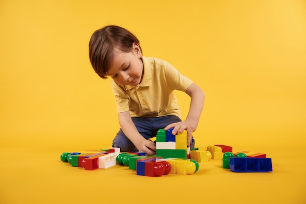 Boy plays with plastic toy bricks. Children leisure concept.