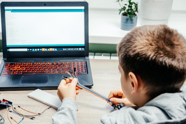 Arduinoのコーディングとロボット工学を学びながらセンサーチップにケーブルを接続する少年